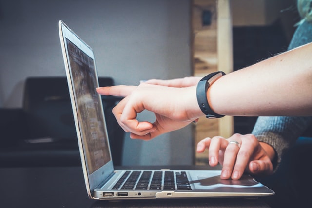 A man's hand pointing to the laptop screen